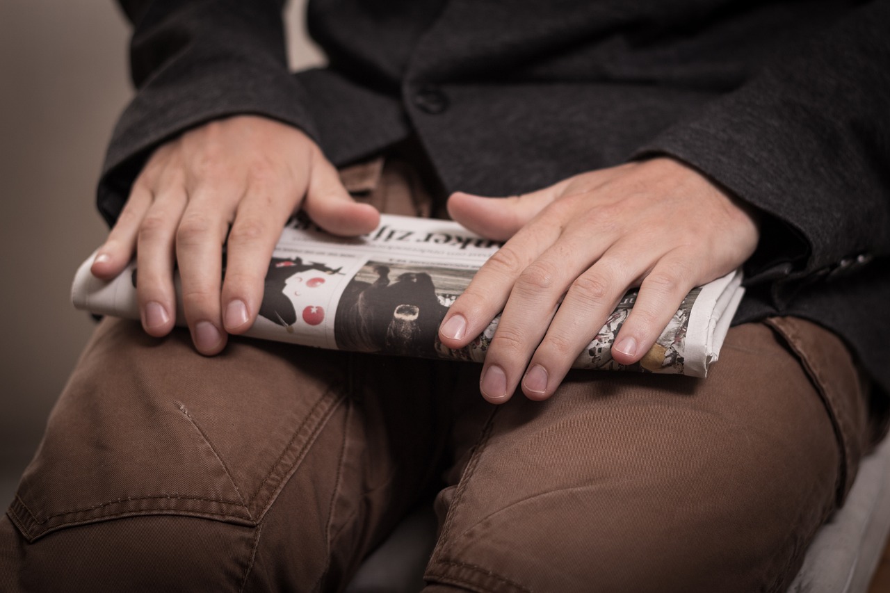 a close up of a person holding a newspaper, sitting with wrists together, aleksander rostov, typical cryptocurrency nerd, press photos