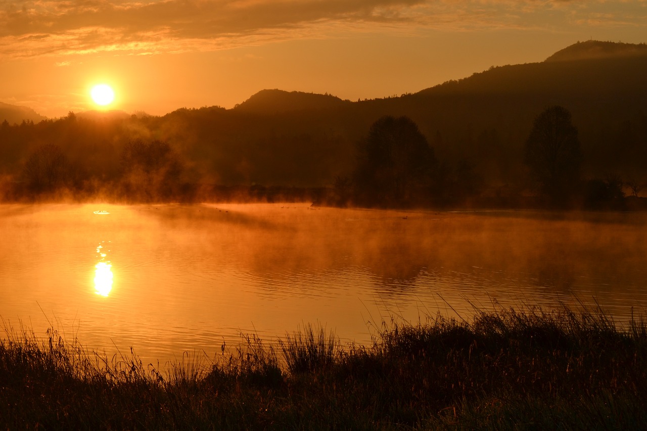 the sun is setting over a body of water, a picture, by Mirko Rački, flickr, romanticism, light orange mist, scenic view of river, steamy, banner
