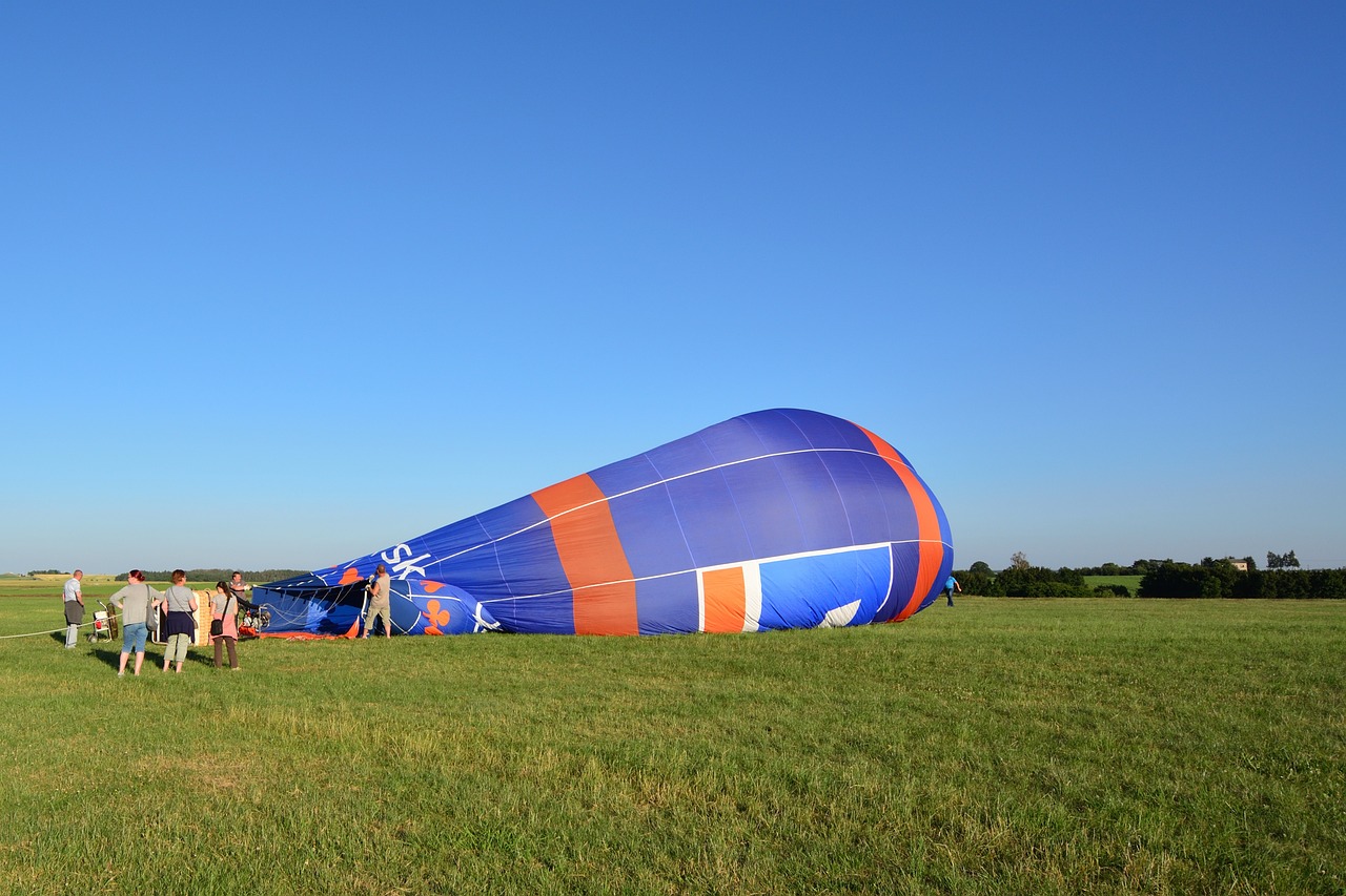 a group of people standing around a hot air balloon, a picture, by Werner Gutzeit, shutterstock, crashed in the ground, view from side, blue and orange, maintenance photo