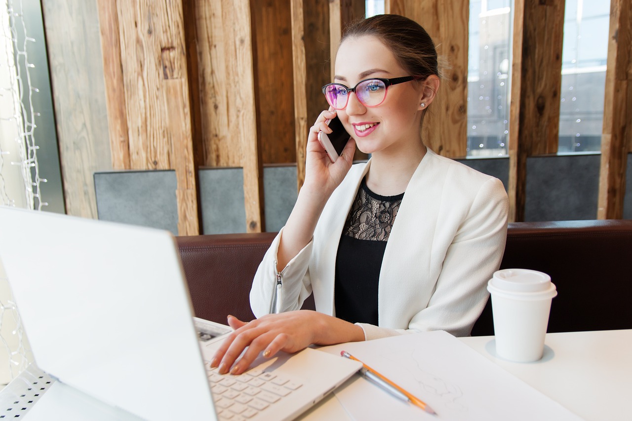 a woman sitting in front of a laptop talking on a cell phone, a portrait, by Rhea Carmi, shutterstock, wearing white suit and glasses, ukrainian, 2019 trending photo, stock photo