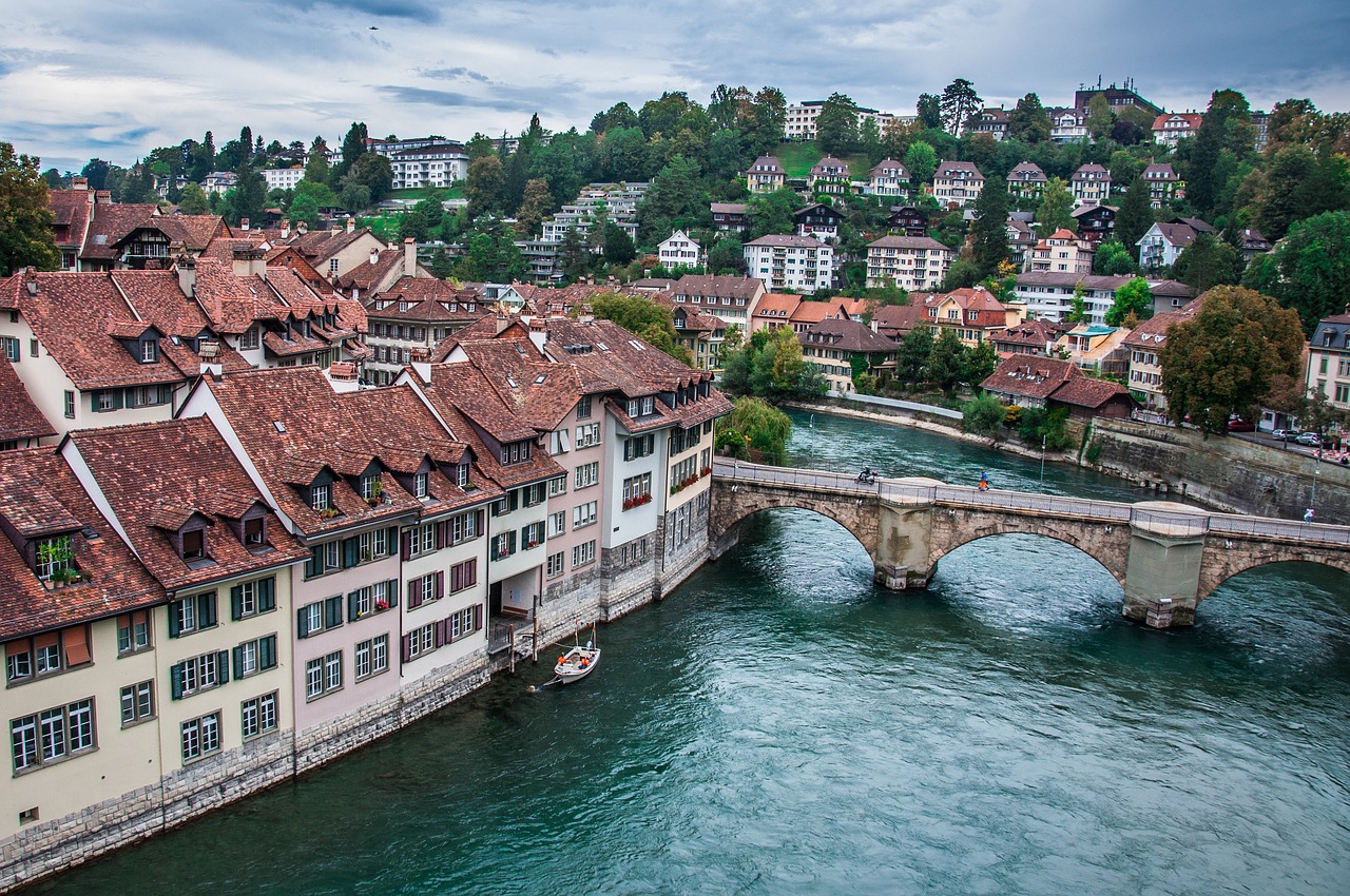 a river running through a town next to a bridge, by Karl Stauffer-Bern, shutterstock, on a cloudy day, red roofs, usa-sep 20, tonemapped