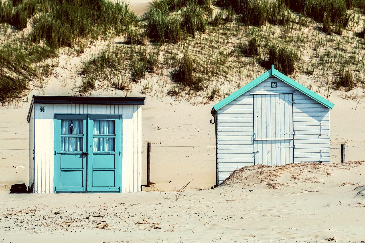 a couple of beach huts sitting on top of a sandy beach, a photo, by Richard Carline, pexels, fine art, doors, white and teal garment, dutch masterpiece, tiny house