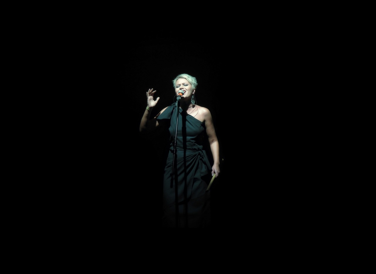 a woman in a black dress singing into a microphone, minimalism, jamie lee curtis, paris 2010, sandy green, dramatic low lighting