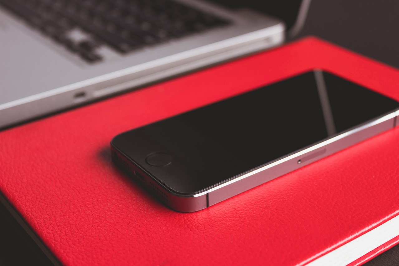 a cell phone sitting on top of a red book, pexels, iphone 15 background, red - black, desk, medium closeup