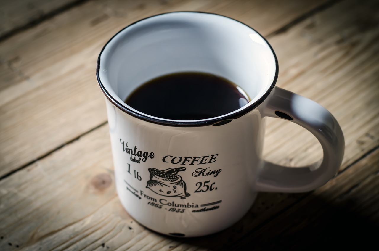 a cup of coffee sitting on top of a wooden table, a photo, by Thomas Häfner, shutterstock, vintage old, white mug, close-up product photo, black