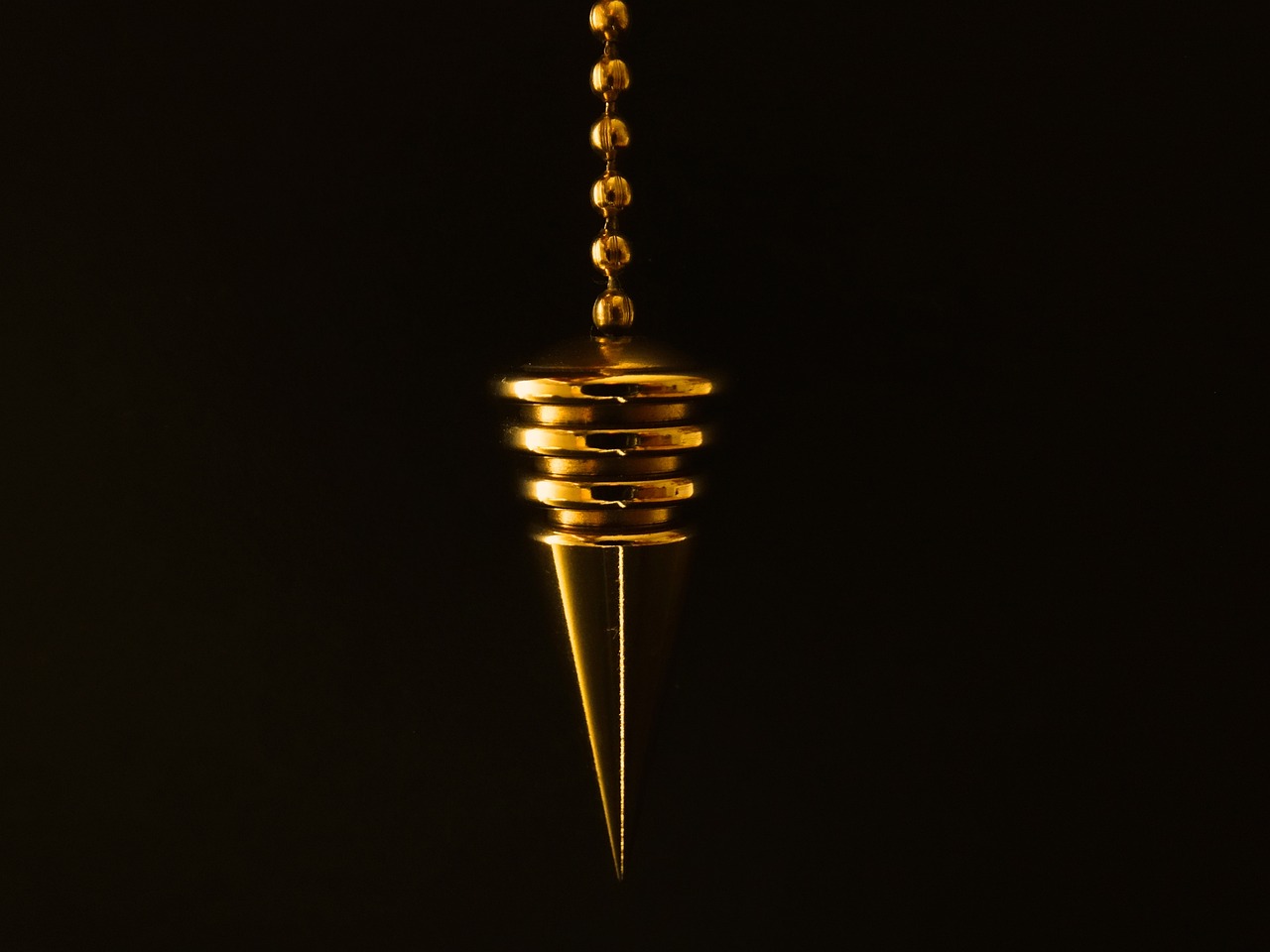 a close up of a gold object on a black background, inspired by Kanō Hōgai, spiked, pendants, miniature product photo, cone shaped