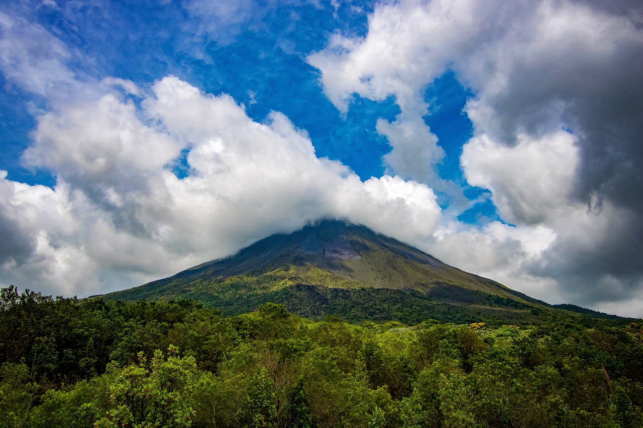a large mountain surrounded by trees under a cloudy sky, a photo, by Juan O'Gorman, volcano background, in a highly detailed jungle, post-processed, summer