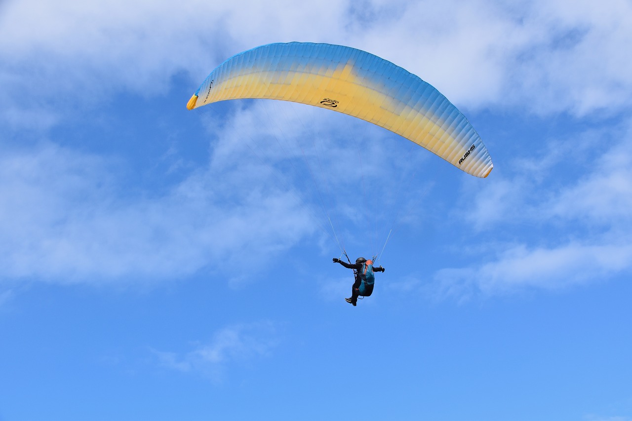 a person that is in the air with a parachute, a picture, by David Burton-Richardson, shutterstock, yellow and blue color scheme, new zeeland, ornithopter, light blue sky with clouds