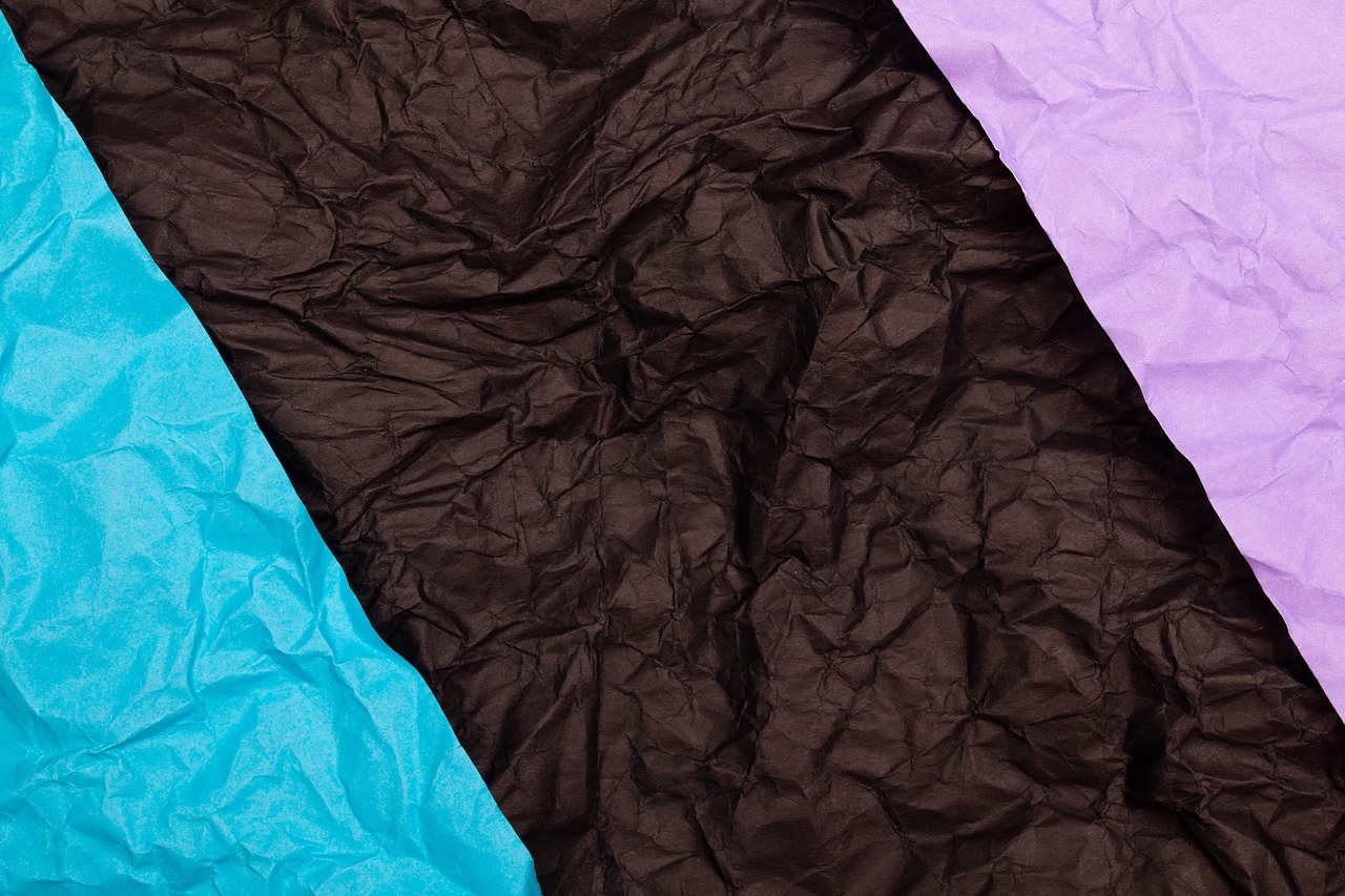 a close up of two different colored sheets of paper, color field, paper crumpled texture, black and blue and purple scheme, brown background, carnival background