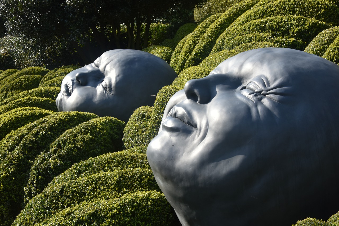a couple of statues sitting on top of a lush green field, by Weiwei, environmental art, macro head face, with soft bushes, world of sleepers, turning her head and smiling