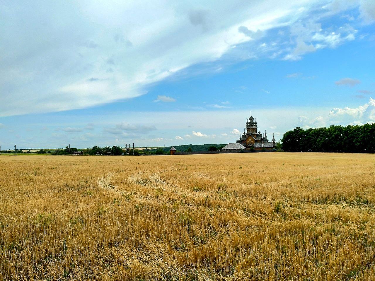 a field of brown grass with a church in the background, by Serhii Vasylkivsky, flickr, immense wheat fields, side view from afar, monastery, magnificent super wide angle