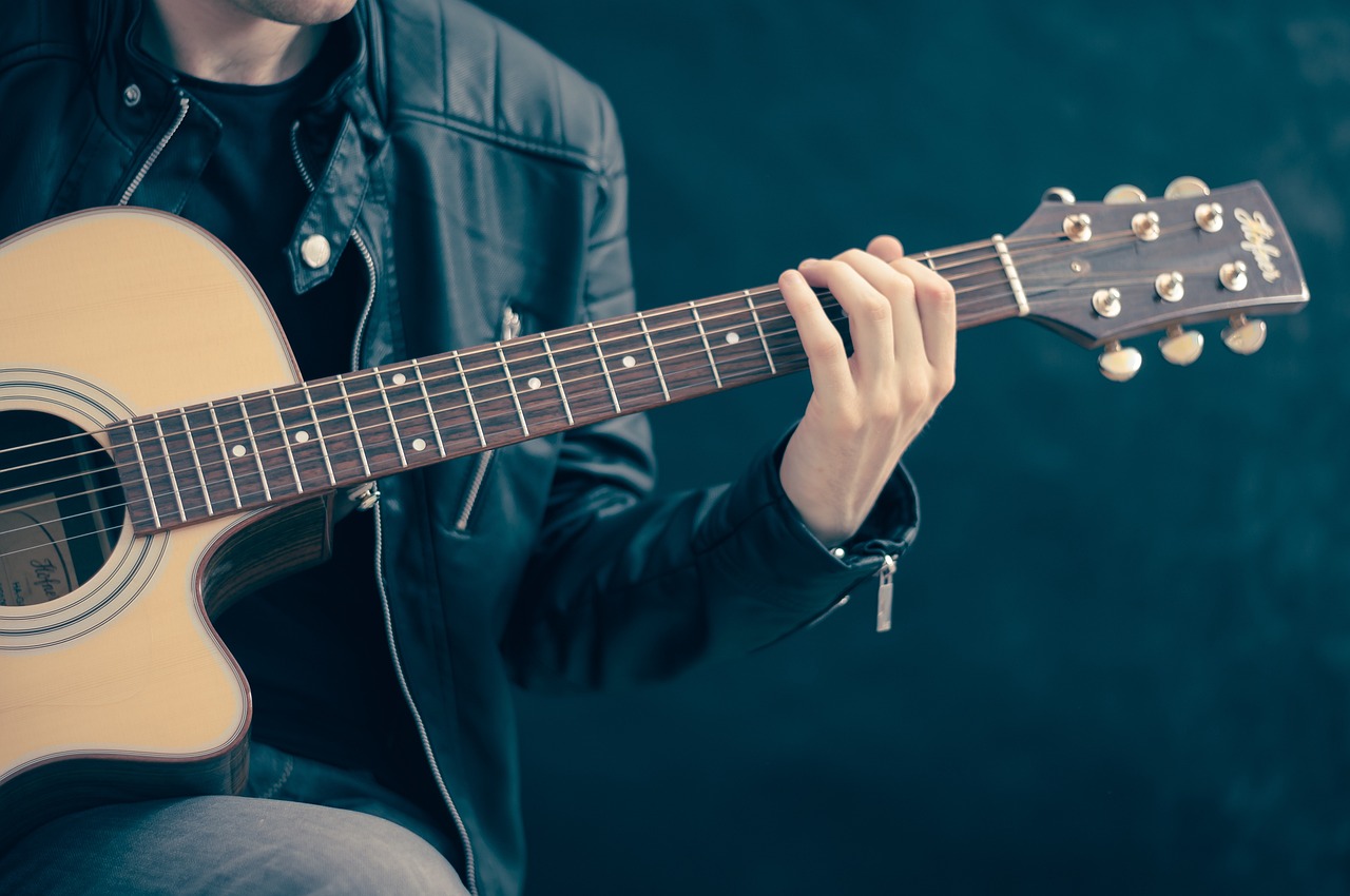a close up of a person playing a guitar, inspired by James Bard, pexels, realism, wearing a leather jacket, avatar image, stage, acoustic information