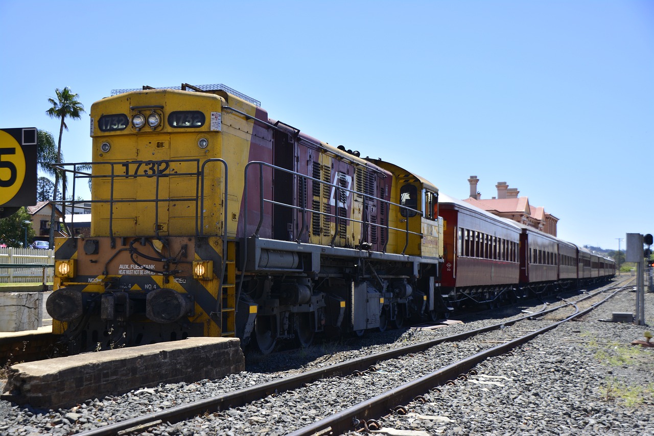 a yellow and red train traveling down train tracks, by Lee Loughridge, shutterstock, on a hot australian day, diesel engine, mule, train station