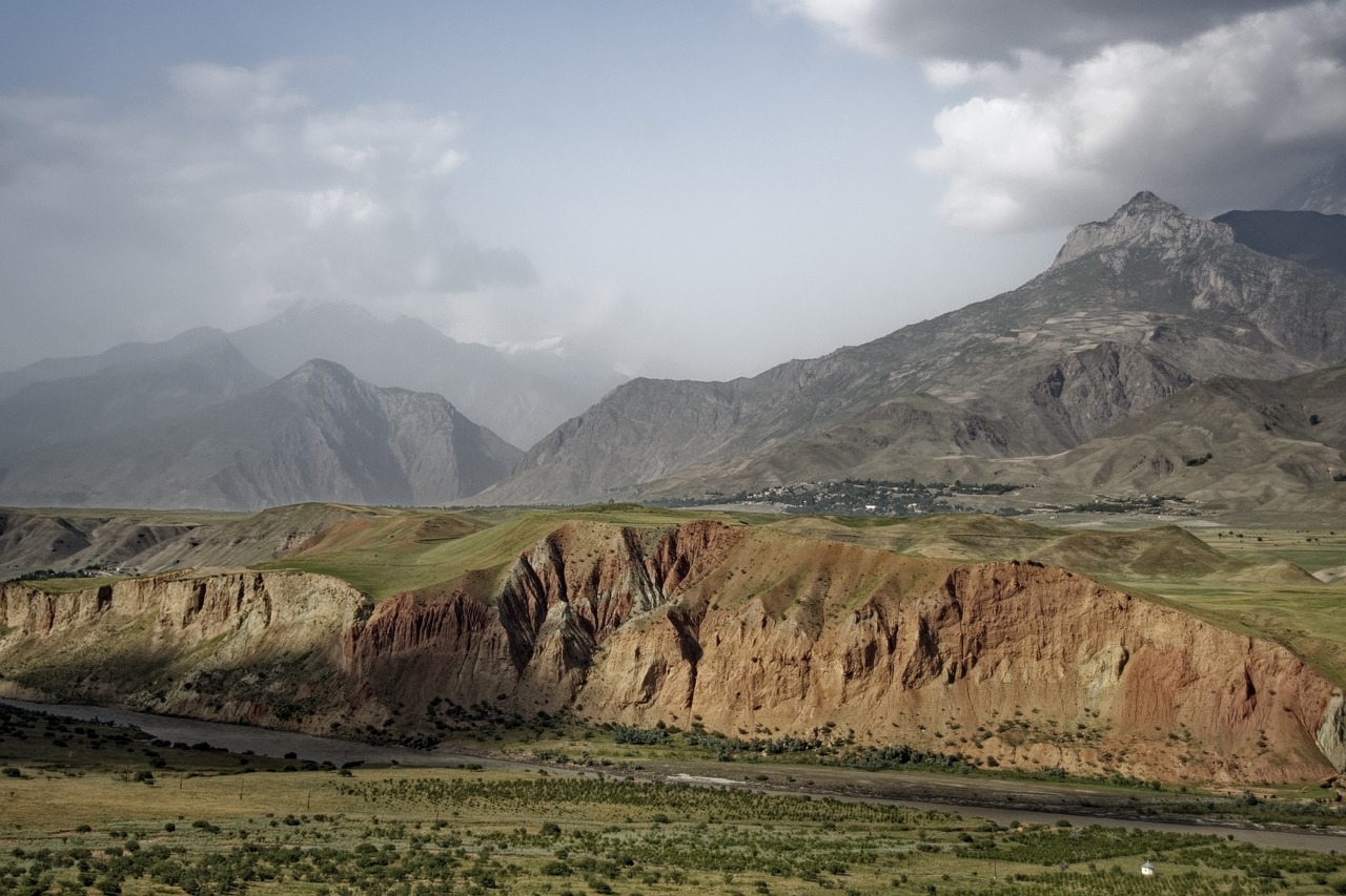 a view of a valley with mountains in the background, by Muggur, pexels contest winner, hurufiyya, between sedimentary deposits, color and contrast corrected, wind and dust, slight overcast weather