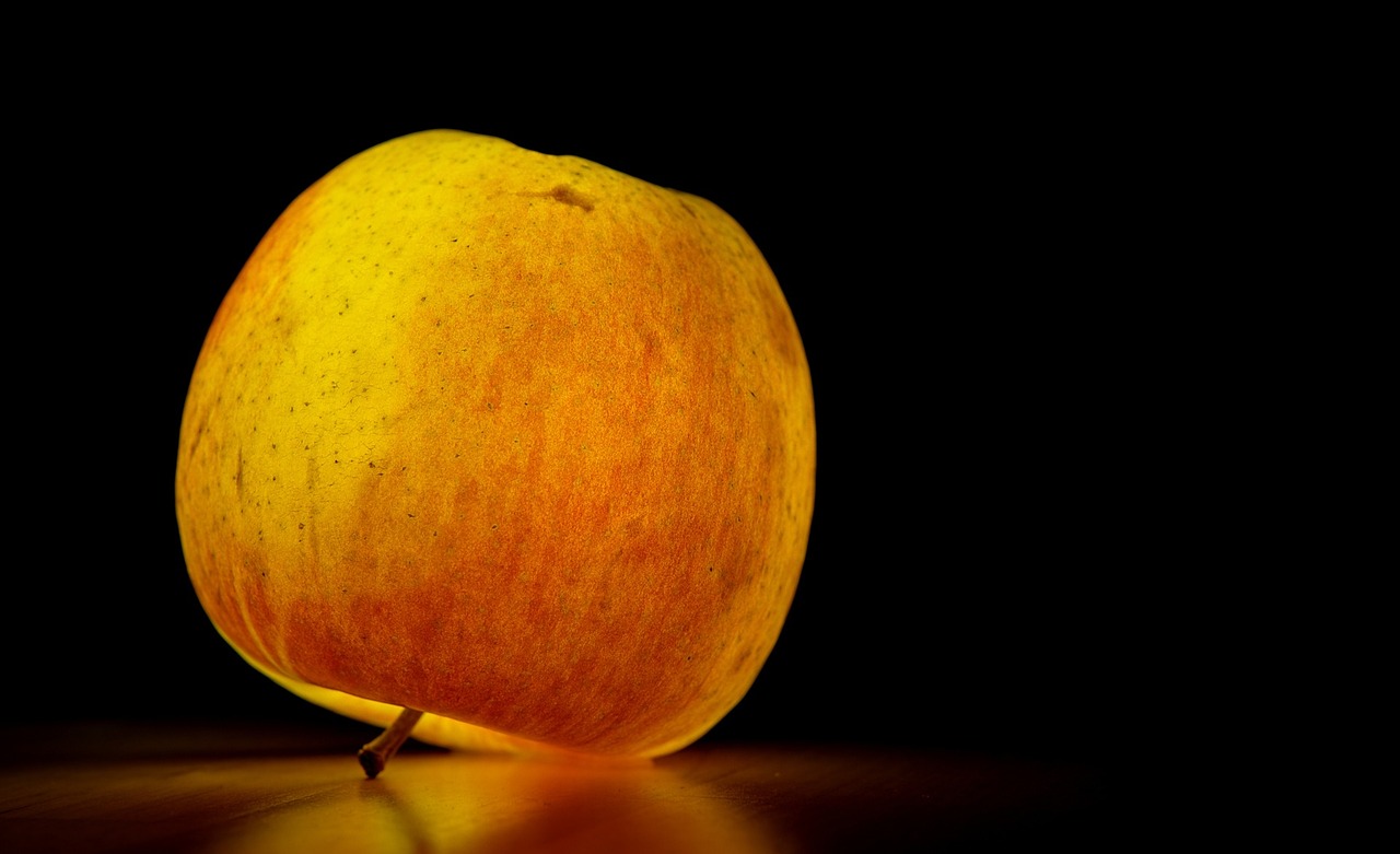 a yellow apple sitting on top of a table, a macro photograph, inspired by Orazio Gentileschi, orange neon backlighting, hd wallpaper, gourd, slightly turned to the right