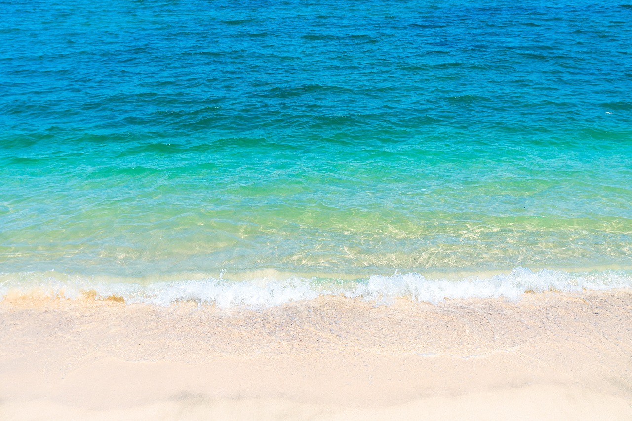 a large body of water sitting on top of a sandy beach, a picture, shutterstock, background image, cerulean, wallpaper - 1 0 2 4, sapphire waters below