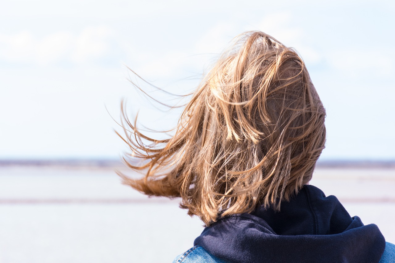 a woman standing in front of a body of water, happening, windy hair, back of head, boy hair, istock