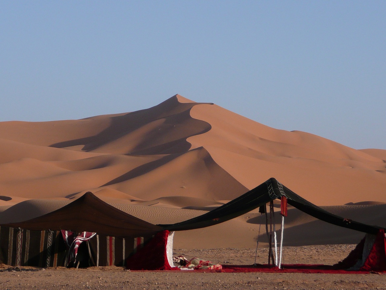 a tent set up in the middle of a desert, by Robert Brackman, flickr, hurufiyya, dunes in the background, red!! sand, canopies, sand - colored walls