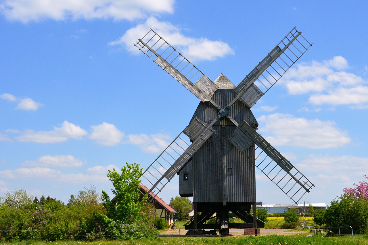 a windmill sitting on top of a lush green field, a picture, by Jörg Immendorff, wooden structures, it is very huge, on a bright day, vacation photo