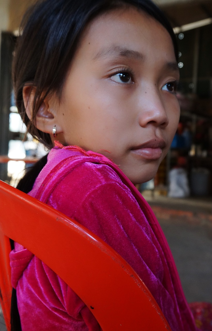 a little girl sitting on top of a red chair, flickr, hurufiyya, laos, closeup of face, long ears, market