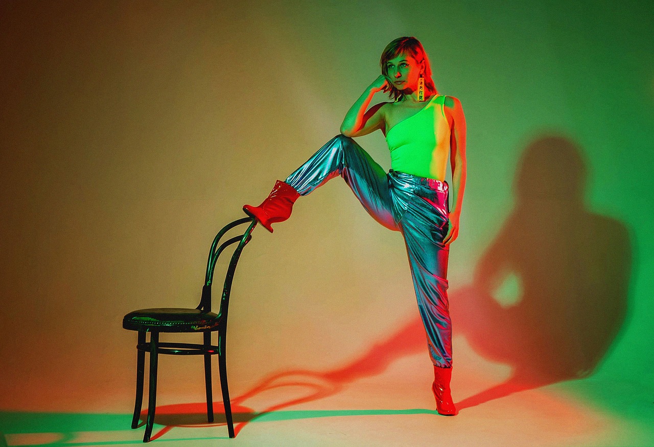 a woman sitting on top of a chair next to a chair, by Emma Andijewska, colored lighting, red boots, shiny colorful, aurora aksnes and zendaya