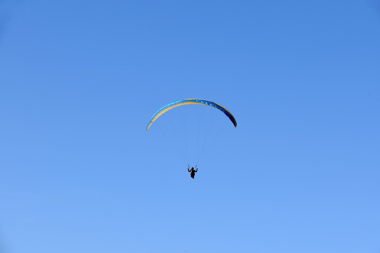 a person that is in the air with a parachute, by Niko Henrichon, flickr, cloudless blue sky, ornithopter, shot from far away, blue backlight