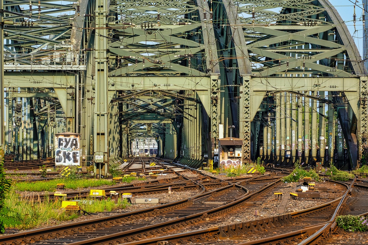 a train traveling down train tracks next to a bridge, a portrait, by Carl Rahl, huge support buttresses, complex composition!!, postprocessed, hell gate