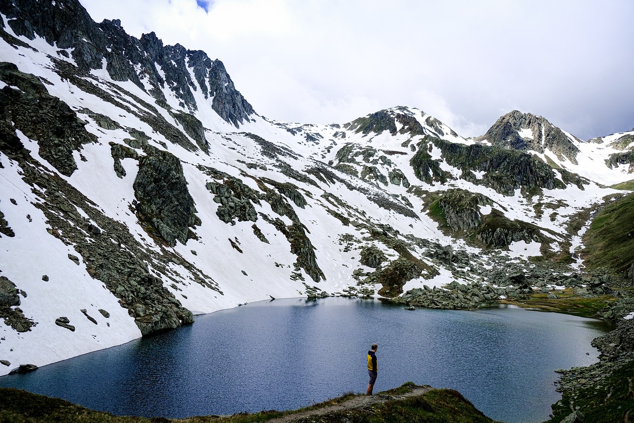 a man standing on top of a mountain next to a lake, a photo, by Werner Andermatt, traveling in france, majestic snowy mountains, summer day, near a small lake