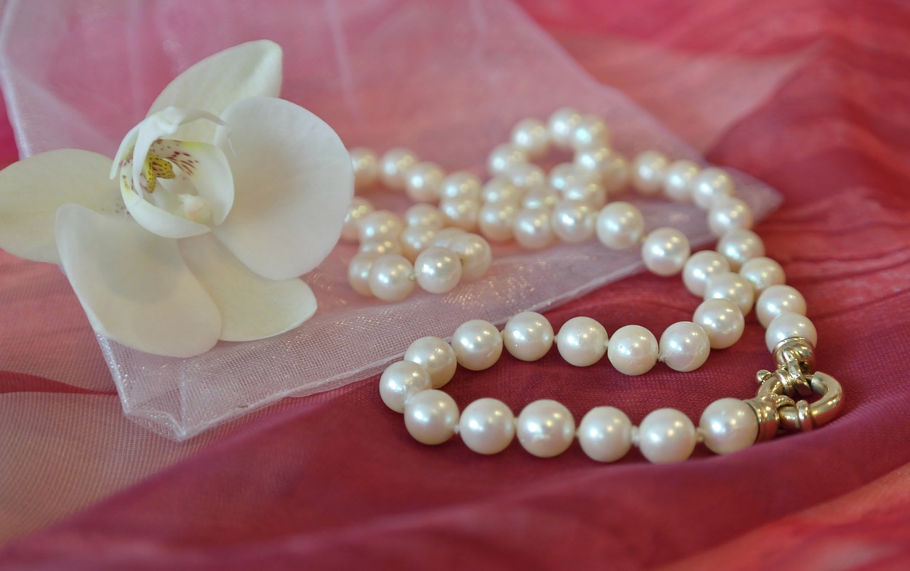 a close up of a necklace with pearls and a flower, by Sylvia Wishart, pixabay, art deco, on a sumptuous tablecloth, orchid, wearing greek palla, soft white glow