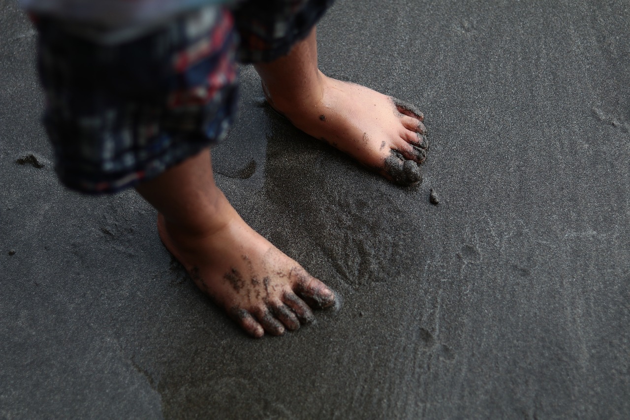 a close up of a person's feet in the sand, a tattoo, realism, sticky black goo, little kid, gray skin. grunge, taiwan