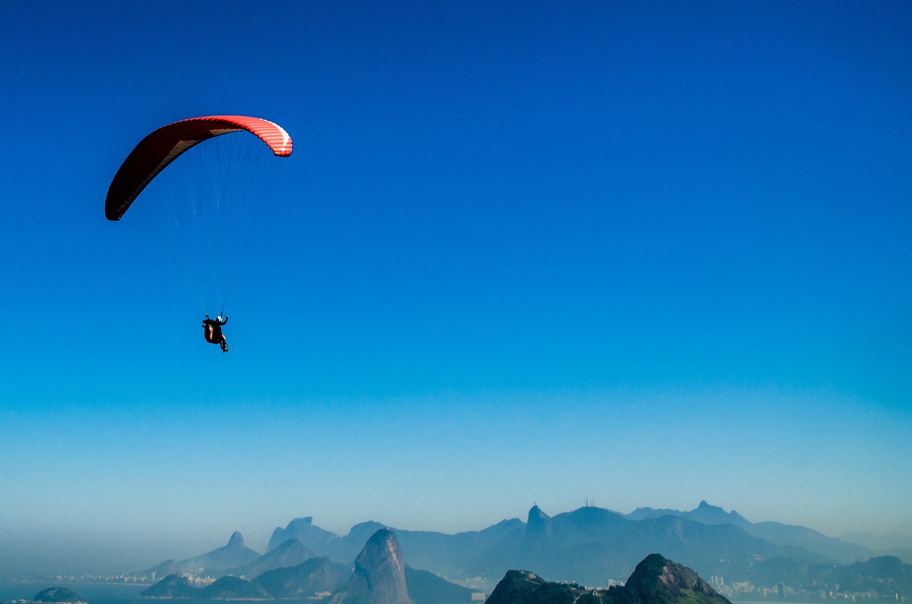 a person flying a kite with mountains in the background, a picture, by Niko Henrichon, rio de janeiro, banner, skydiving, parallax »