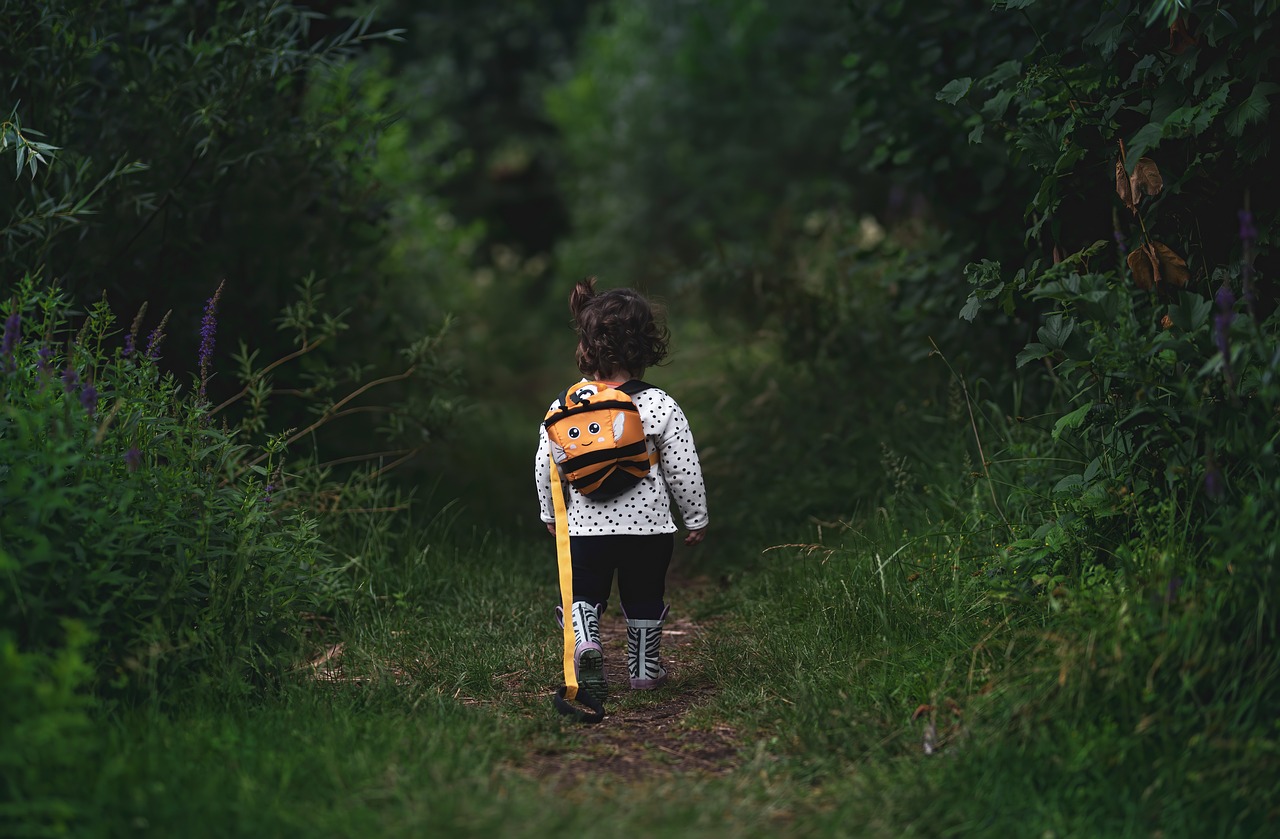 a little girl with a backpack walking down a path, by Jesper Knudsen, 🤬 🤮 💕 🎀, with yellow cloths, on a dark swampy bsttlefield, student