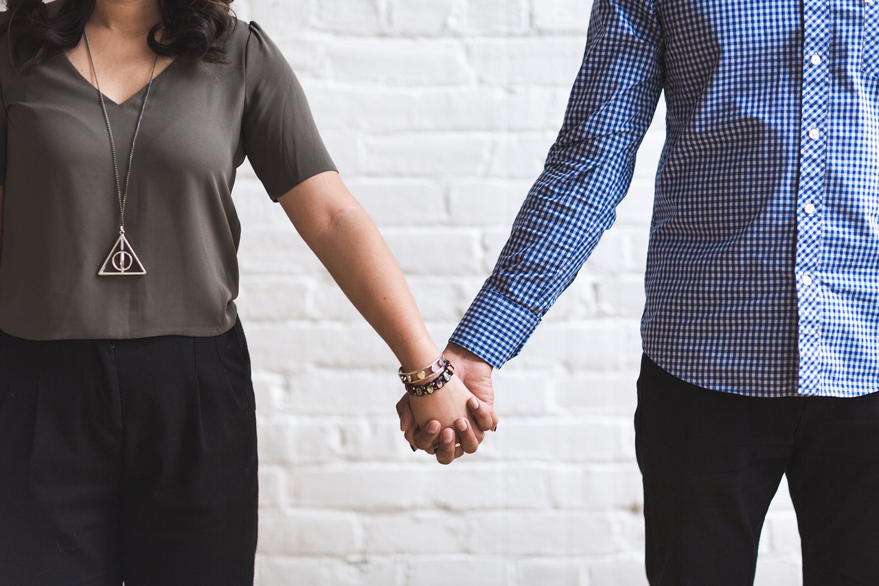 a man and a woman holding hands in front of a white brick wall, office clothes, holding each other hands, no cutoff, wife