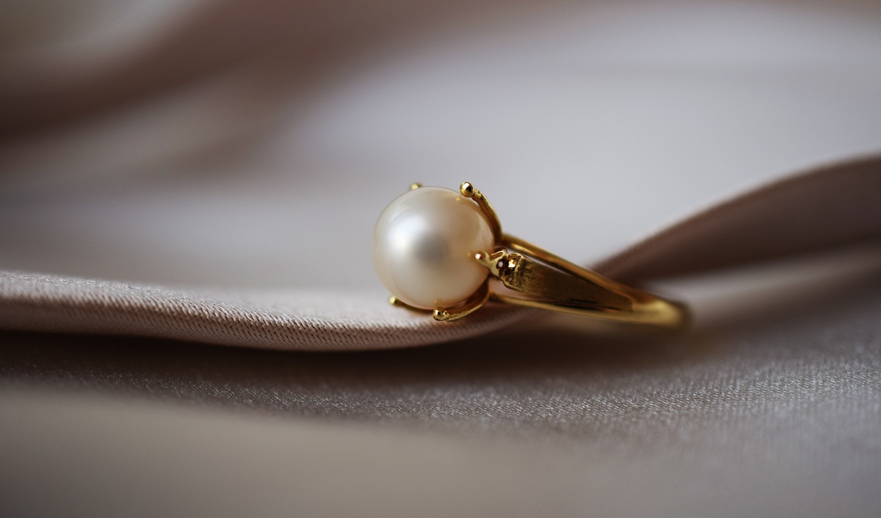 a pearl ring sitting on top of a white cloth, a macro photograph, inspired by Pieter de Ring, golden detailing, simple yet detailed, hanna moon, 50s