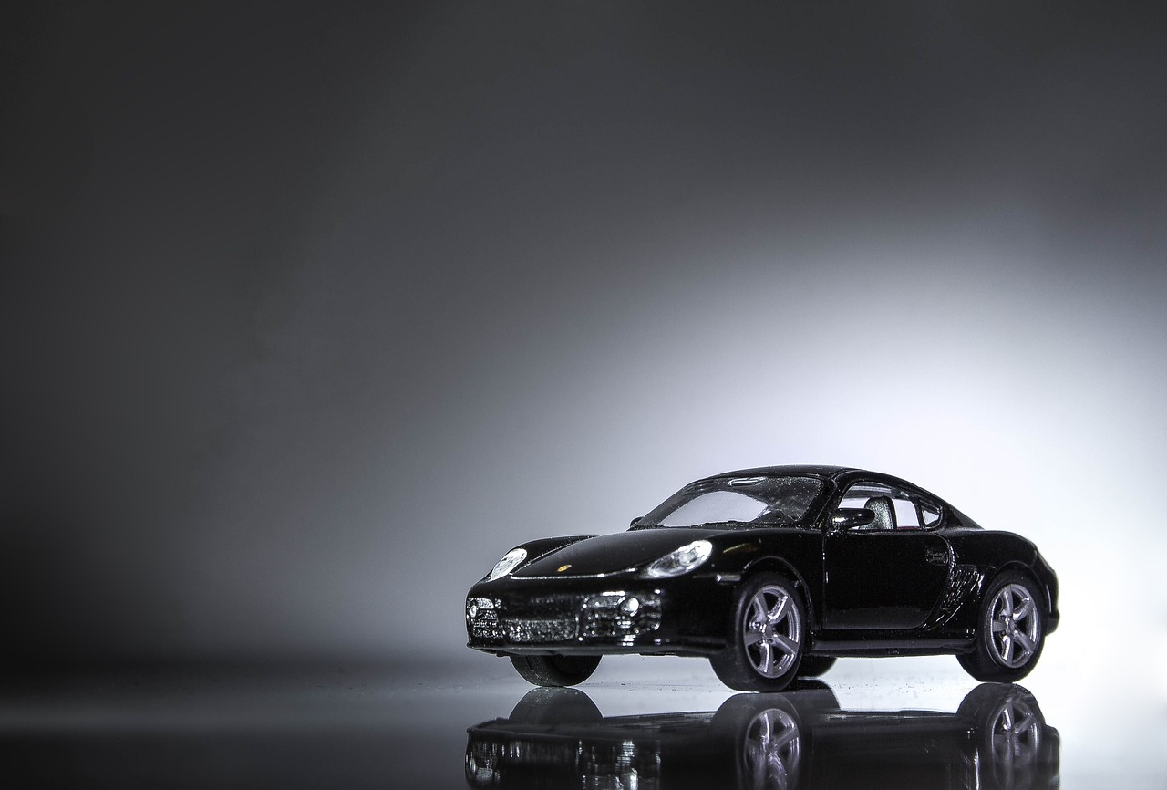 a black toy car sitting on top of a reflective surface, inspired by Harry Haenigsen, porsche 9 1 1, dramatic lighting”, full body wide shot, toy photo