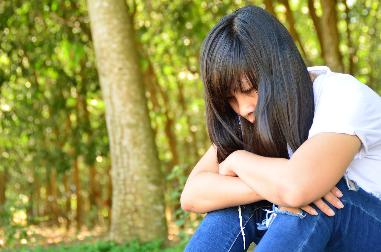 a woman sitting on a bench with her head in her hands, shutterstock, realism, portrait of a japanese teen, sitting in the forrest, with a hurt expression, a beautiful teen-aged girl
