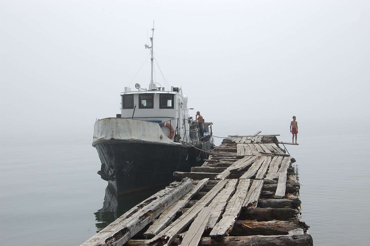 a man standing on a dock next to a boat, by Richard Carline, flickr, fog!, near lake baikal, under repairs, bc