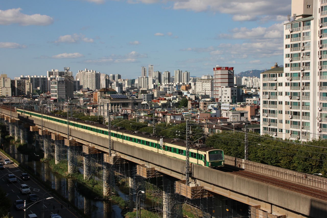 a train traveling over a bridge over a city, by Tanaka Isson, flickr, gwanghwamun, a green, residential area, 6 4 0