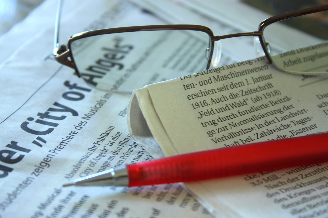 a red pen sitting on top of a newspaper next to a pair of glasses, a picture, by Dietmar Damerau, detailed zoom photo, advertisement, wikimedia, wideangle