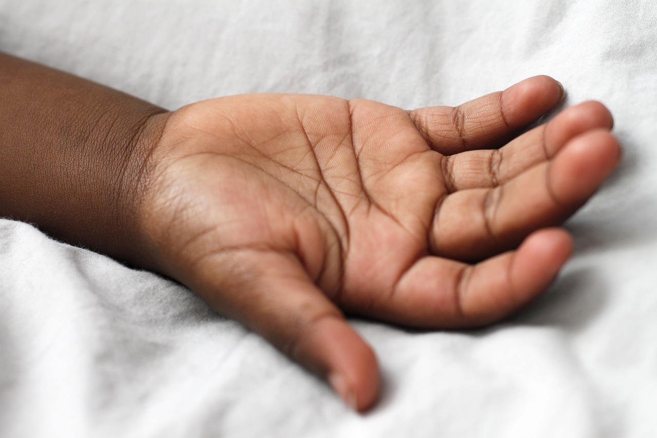 a close up of a person's hand on a bed, hurufiyya, young child, slightly turned to the right, open palm, very dark brown skin!