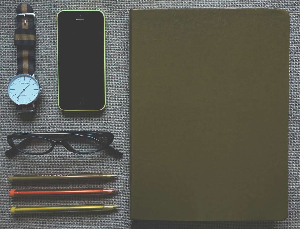 a cell phone sitting on top of a table next to a pair of glasses, a picture, by Andrei Kolkoutine, pexels, minimalism, notebook, green and brown clothes, tools, green and black color scheme