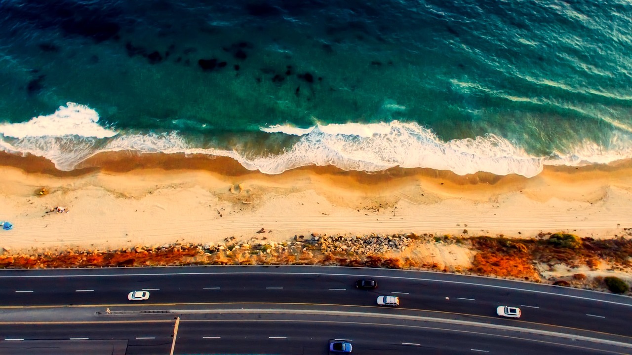 a group of cars driving down a road next to the ocean, by Jacob Steinhardt, pexels contest winner, digital art, sand and sea, southern california, beautiful panoramic imagery, close up shot from the top