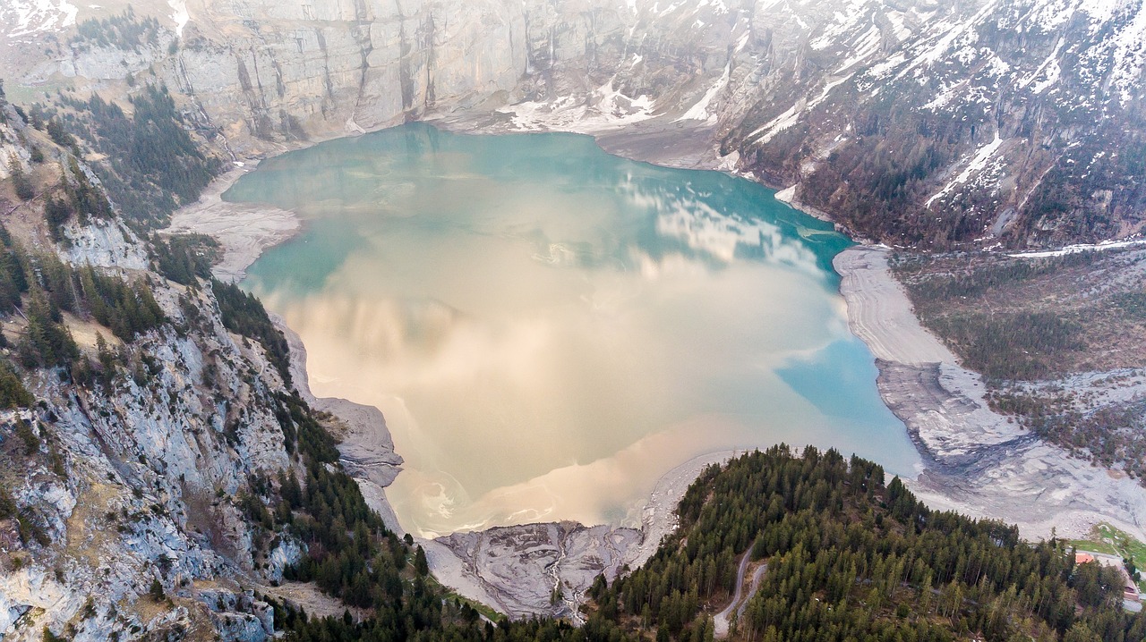 a large body of water surrounded by snow covered mountains, a picture, by Oskar Lüthy, shutterstock, aerial shot from the drone, partly sunken! in the lake!, intense smoldering, benjamin vnuk