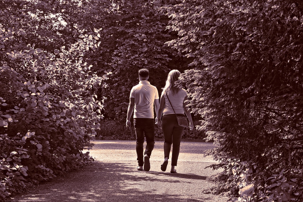 a black and white photo of two people walking down a path, a picture, pexels, romanticism, standing in a botanical garden, boy girl traditional romance, duotone!, hot summer sun