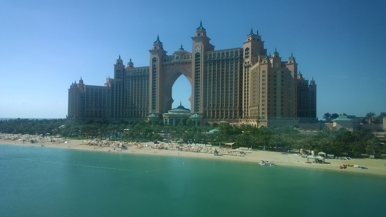 a large building sitting on top of a beach next to a body of water, a picture, atlantis background, full body shot!!, tans, the photo was taken from a boat