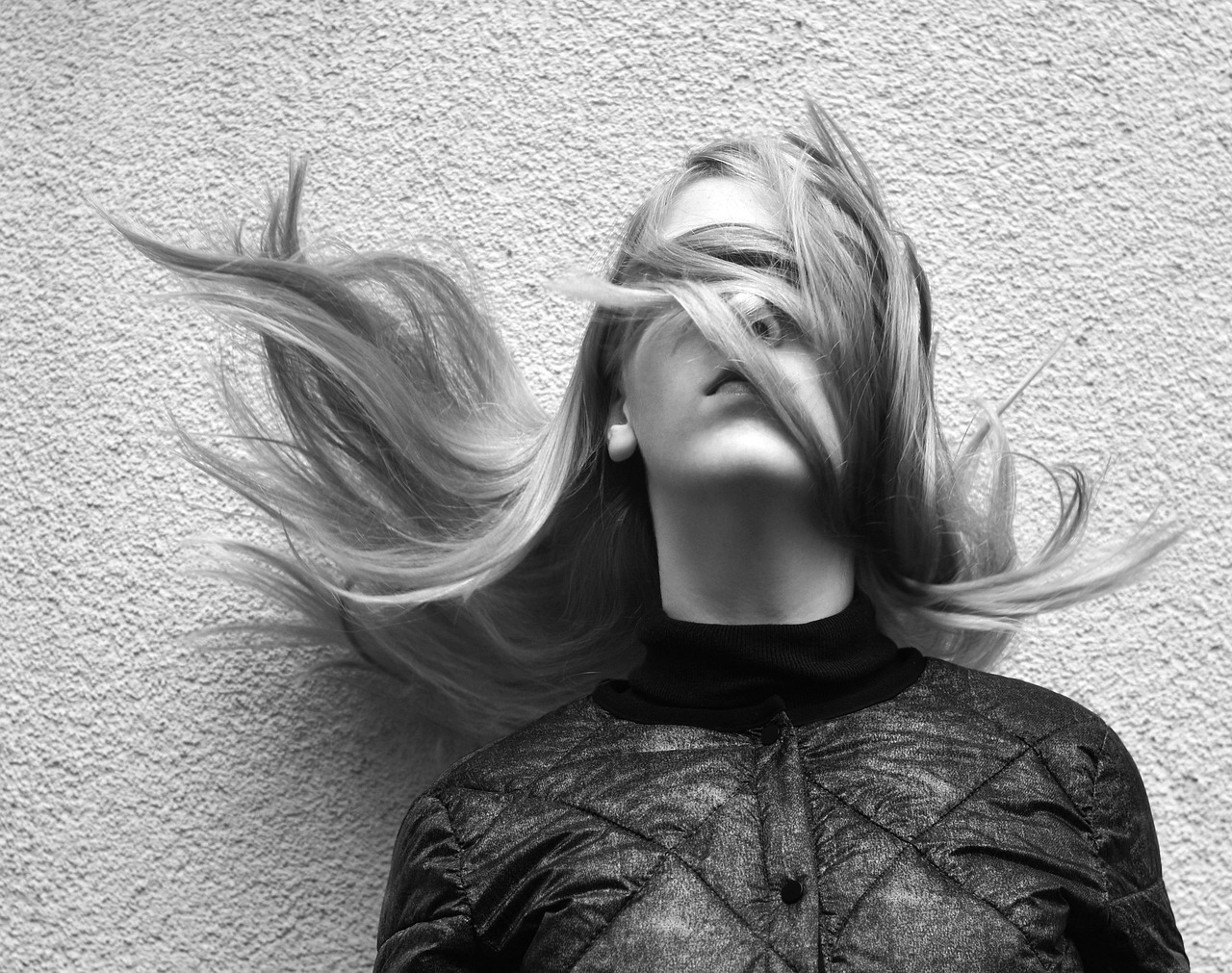 a black and white photo of a woman with her hair blowing in the wind, by Ivana Kobilca, pexels contest winner, realism, tags: blonde hair, laying on her back, long trippy hair, on a wall