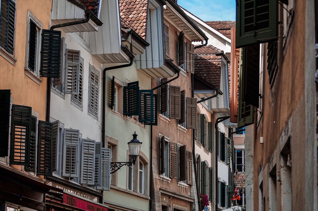 a couple of buildings that are next to each other, a photo, inspired by Karl Stauffer-Bern, shutters, sloped street, portrait!!!!, sunday afternoon