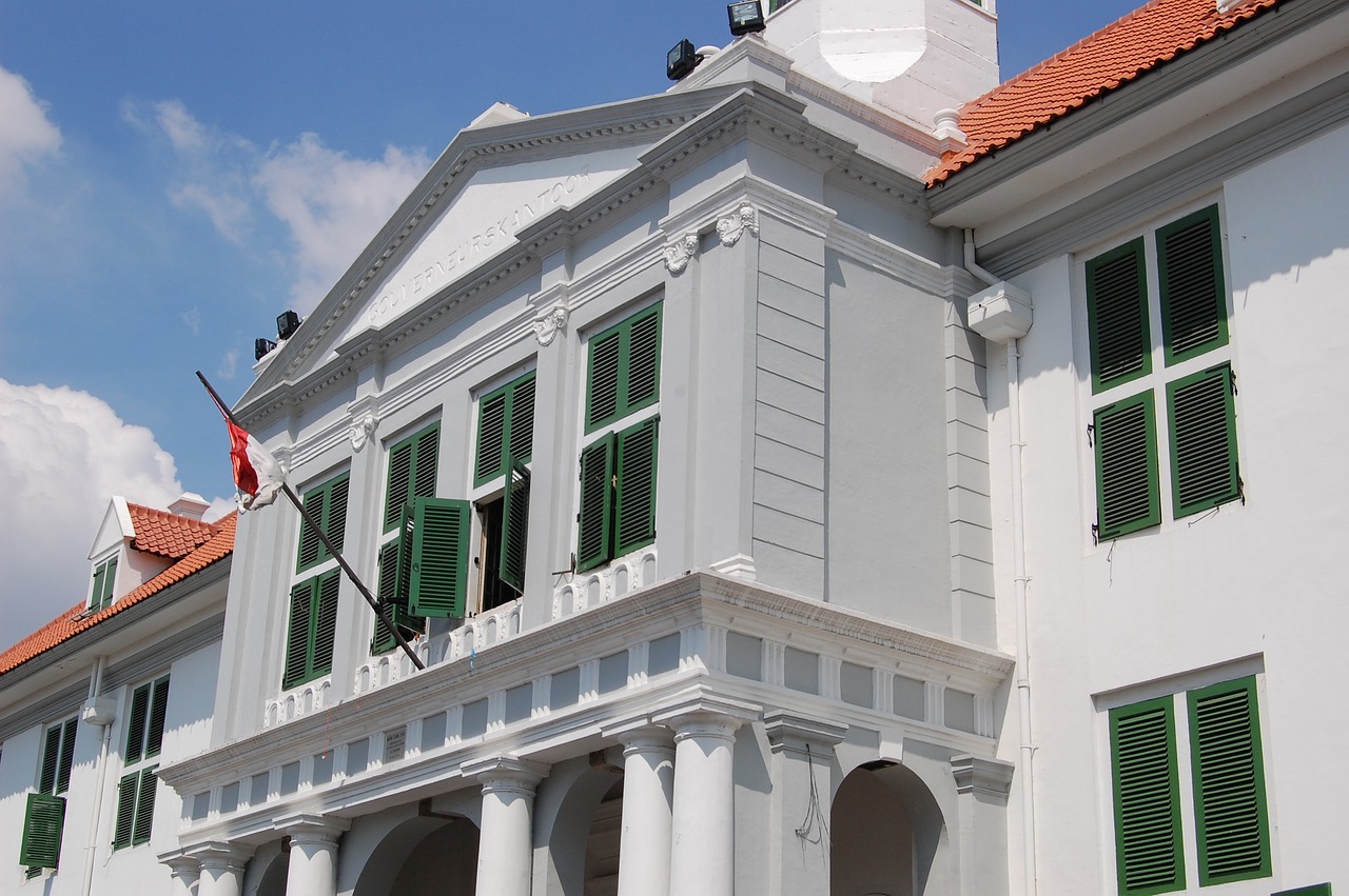 a white building with green shutters and a clock, inspired by João Artur da Silva, jakarta, in balcony of palace, dug stanat, museum