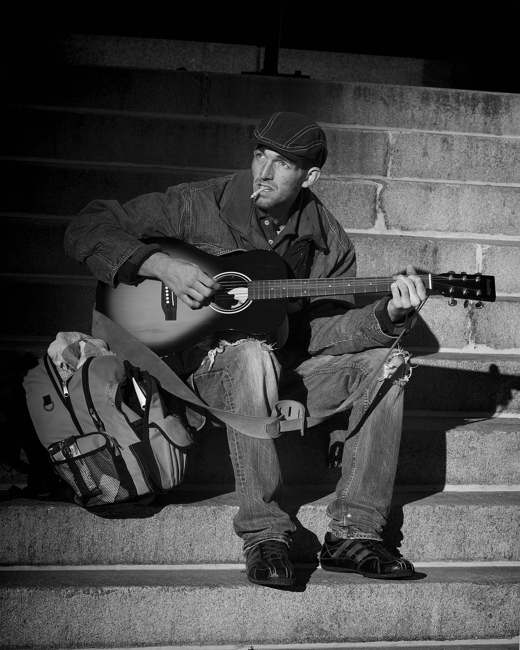 a black and white photo of a man playing a guitar, a photo, inspired by Bruce Gilden, pixabay, sitting on temple stairs, homeless, tim hildebrant, rugged man portrait