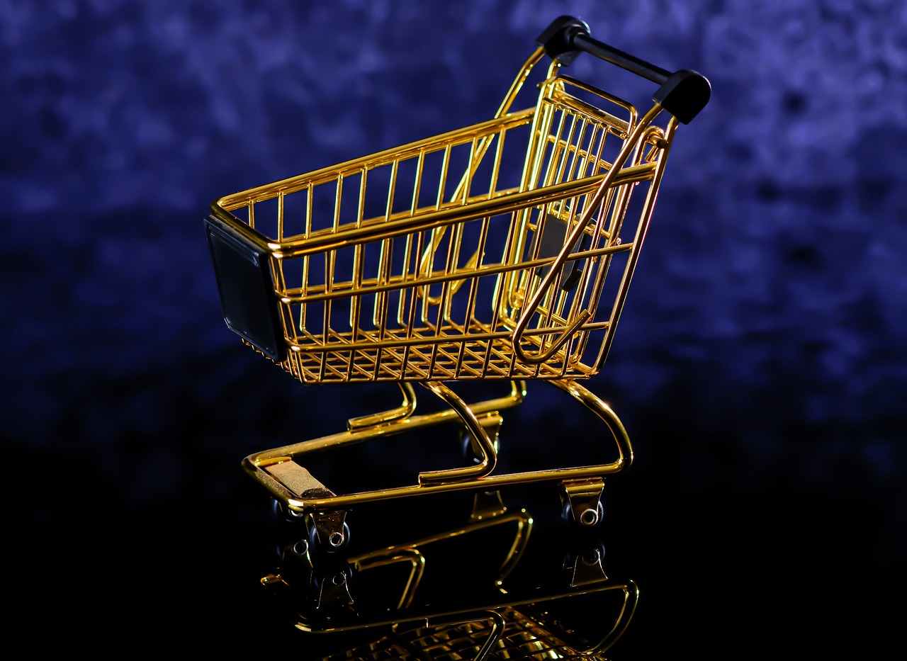 a gold shopping cart sitting on top of a table, modernism, colors with gold and dark blue, with a black background, digital photo, on a reflective gold plate